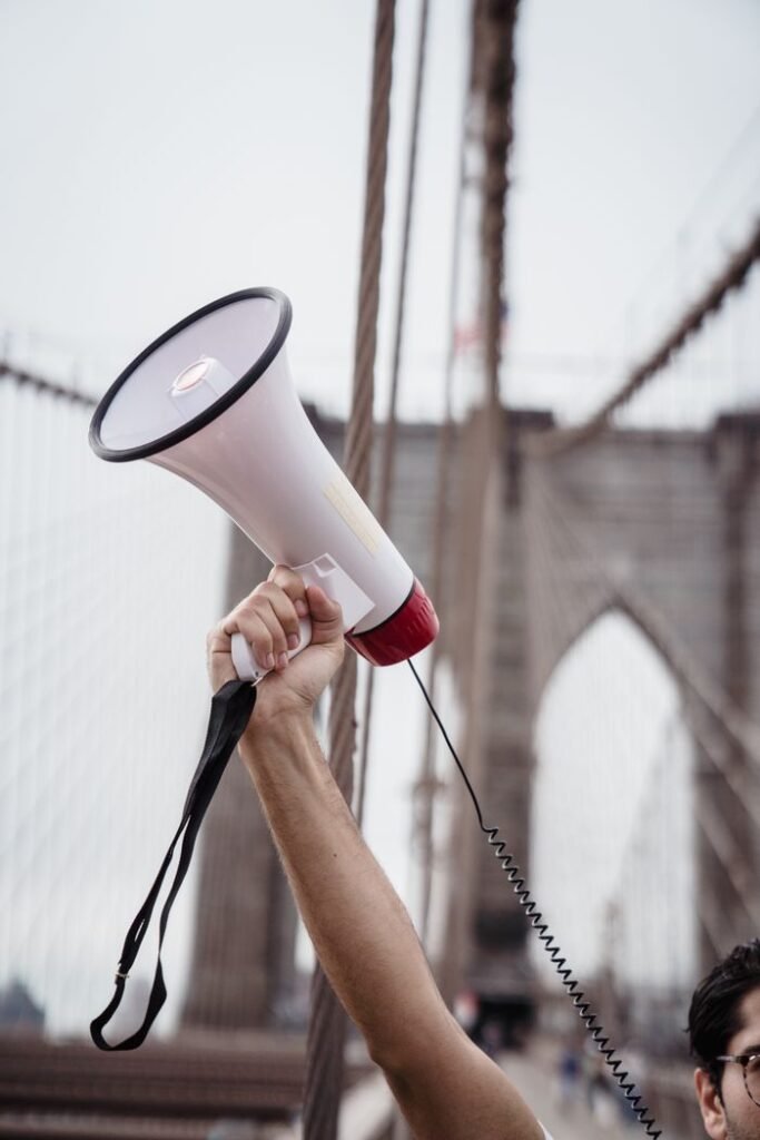 Person holding a megaphone on Brooklyn Bridge symbolizing communication and activism.